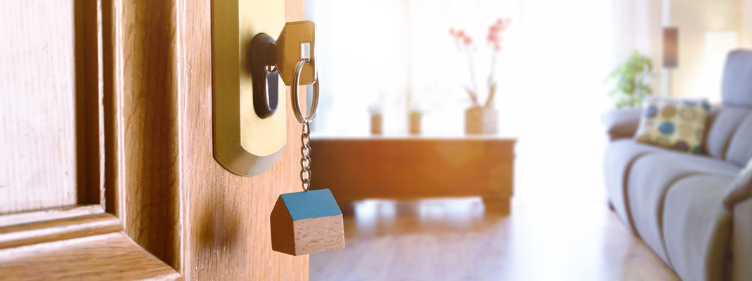 A front door with a keyring hanging from the lock is ajar, showing the inside of a well lit house.